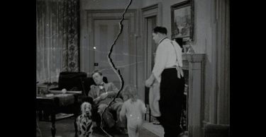 Laurel and Hardy and a toddler in a living room.