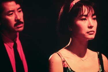 A man standing behind a woman at night.