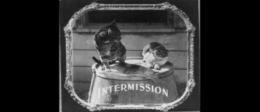 A silent movie title card that reads "Intermission" and depicts two cats on a barrel.
