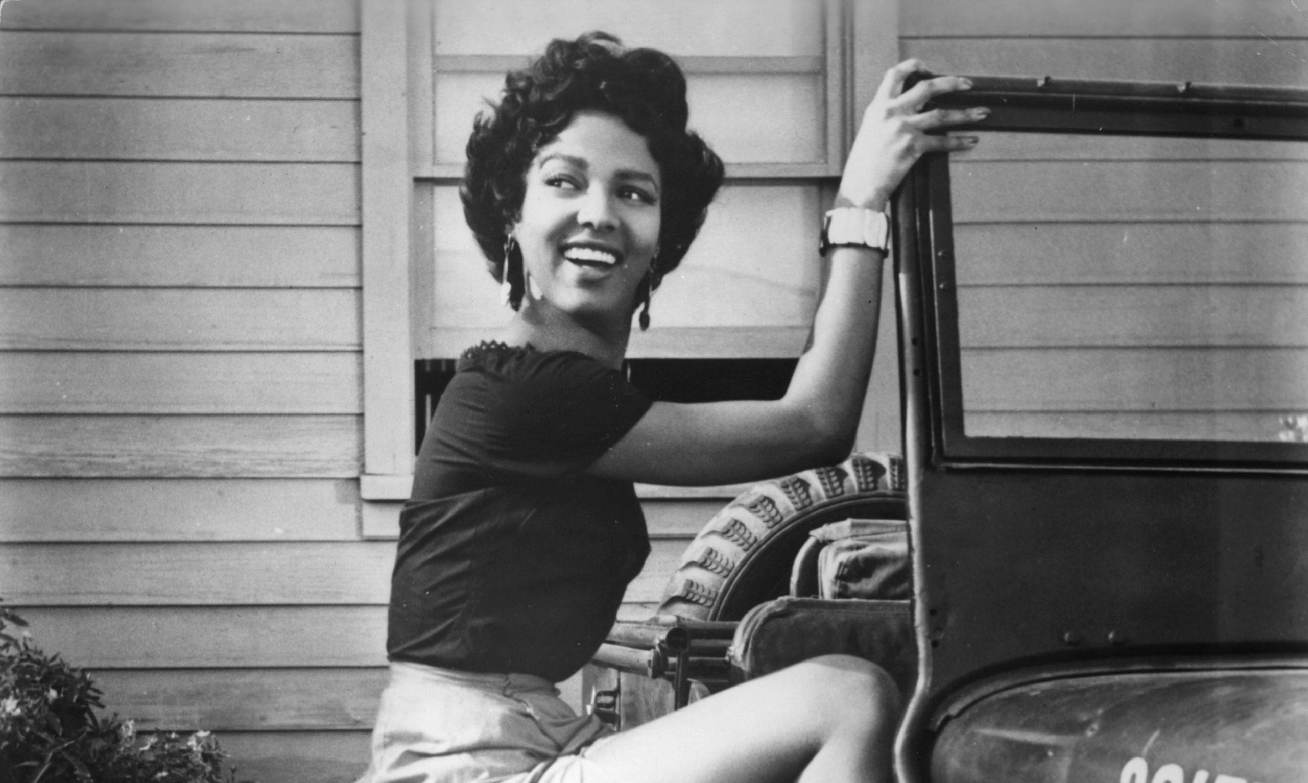 Dorothy Dandridge standing next to a car smiling