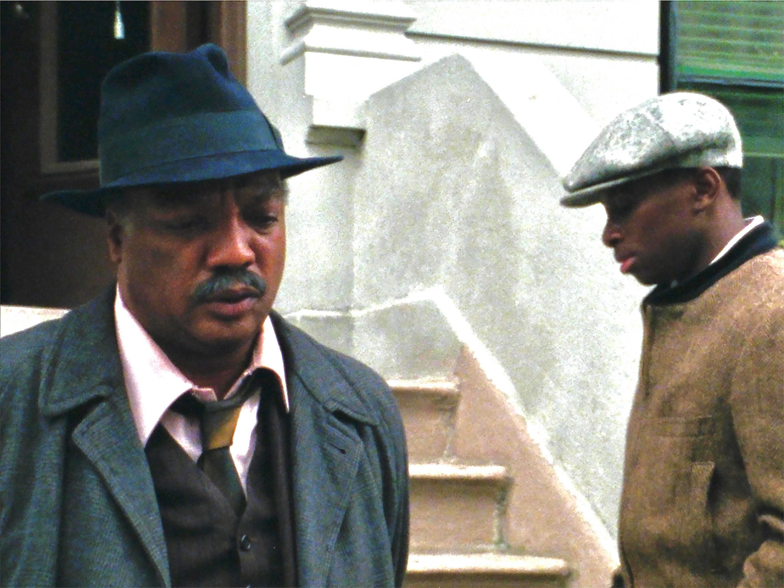 2 men. one is looking away and the other is turned towards the camera, but looking down