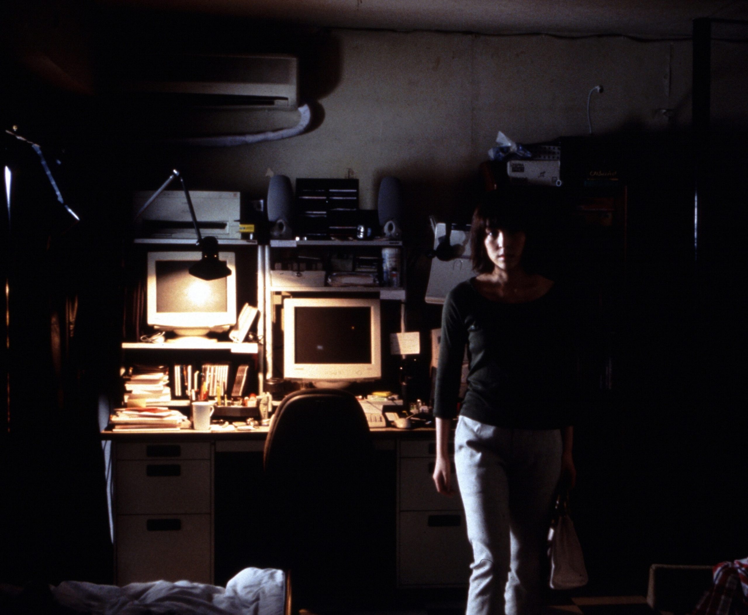 A woman standing in front of a computer desk in a dark room.