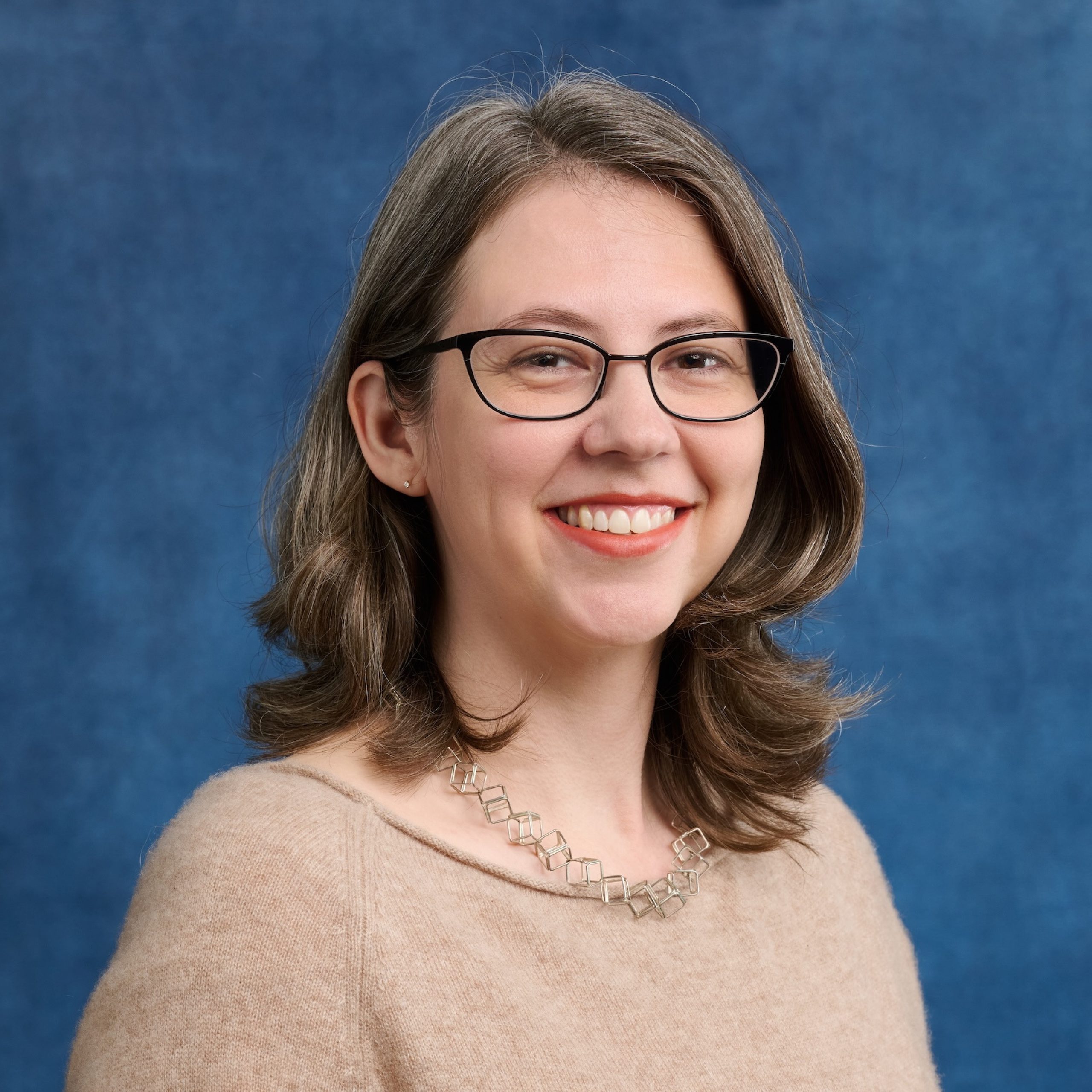 Molly Haigh headshot wearing glasses and light tan top