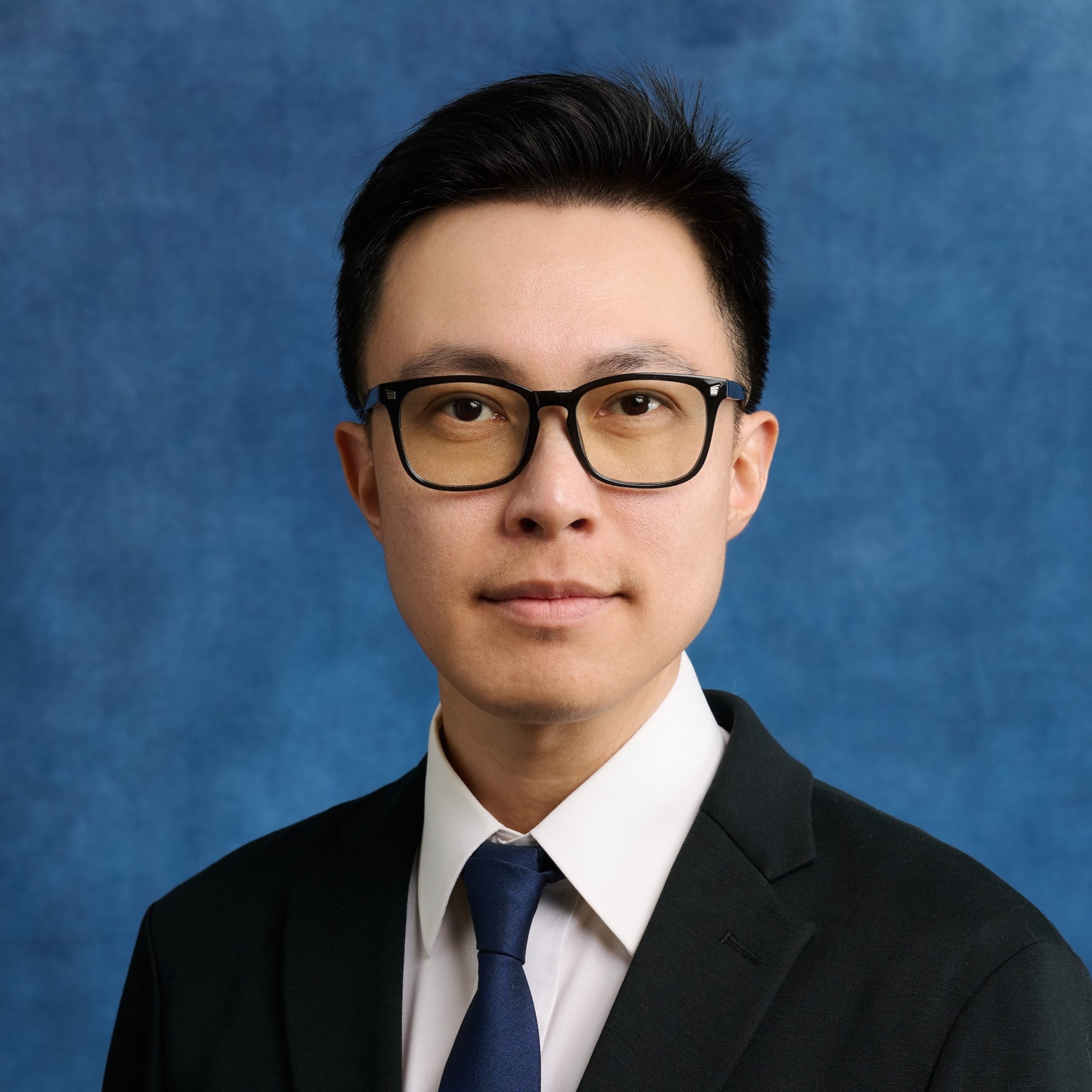 Simon Lee headshot wearing glasses and dark suit and tie