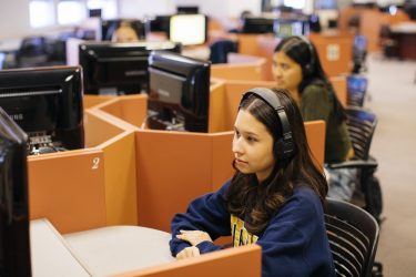 Students looking at monitors and wearing headsets.