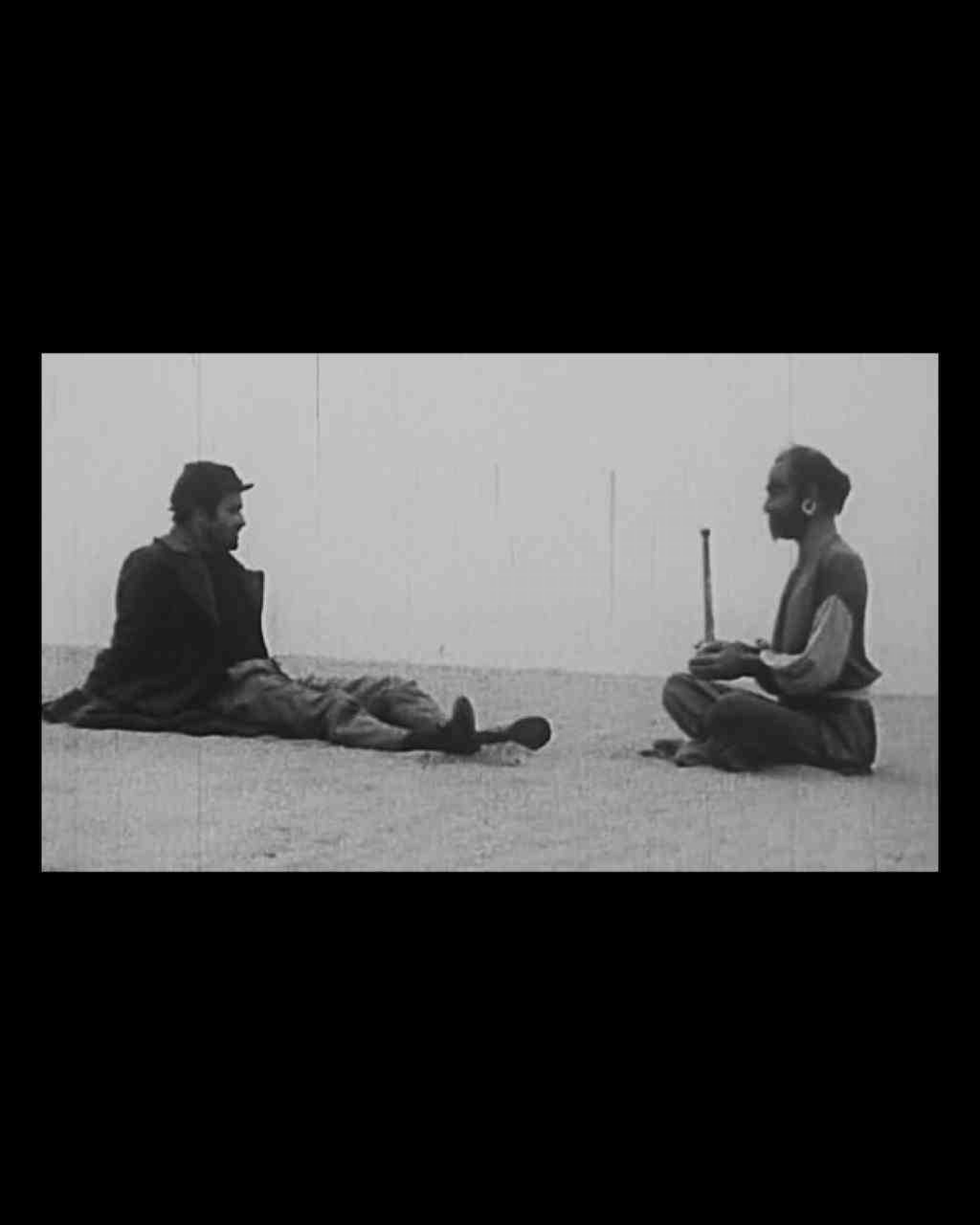 Man reclining on ground facing another man sitting cross-legged