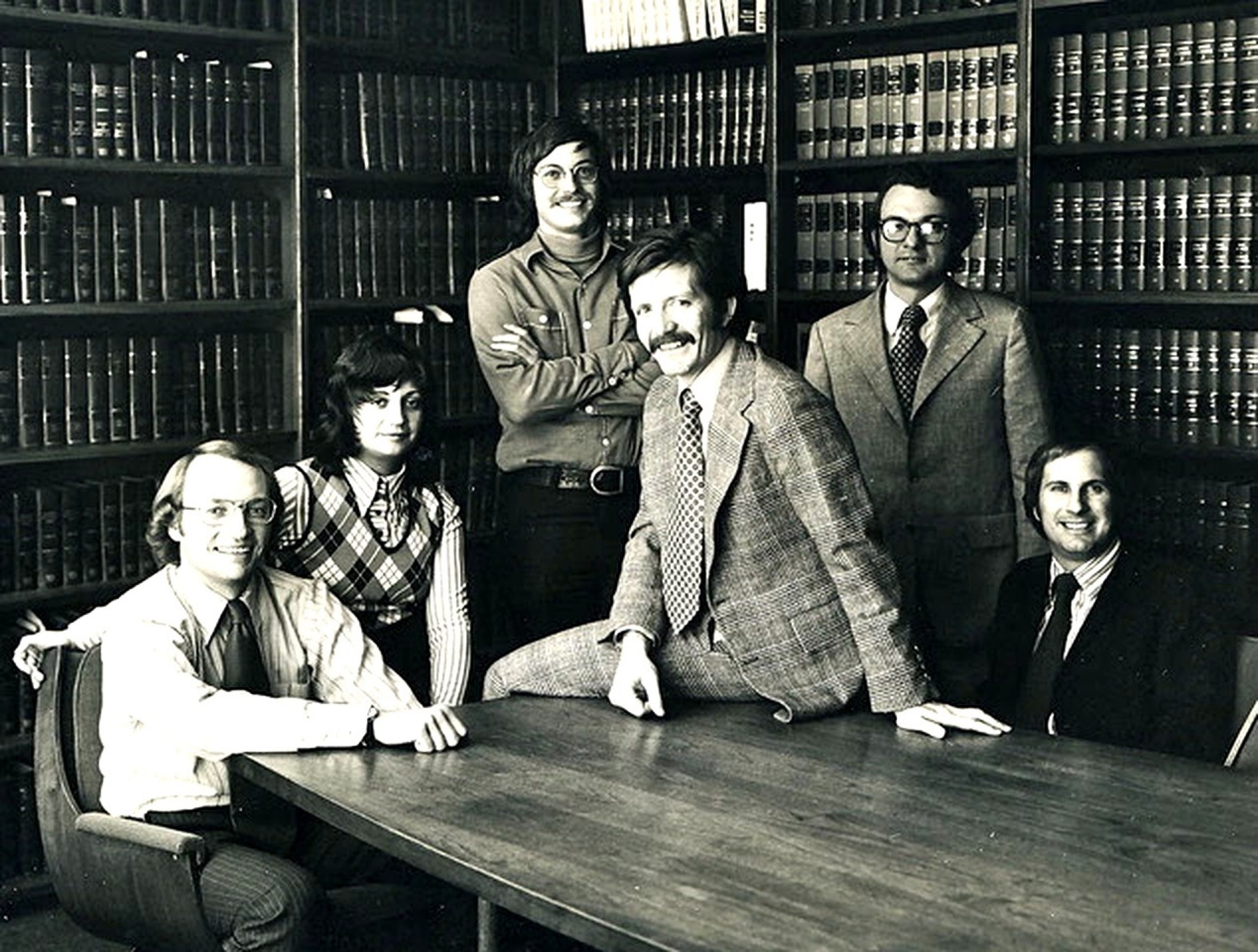 Circe 1974, young lawyers sit and stand around a table inside a library.