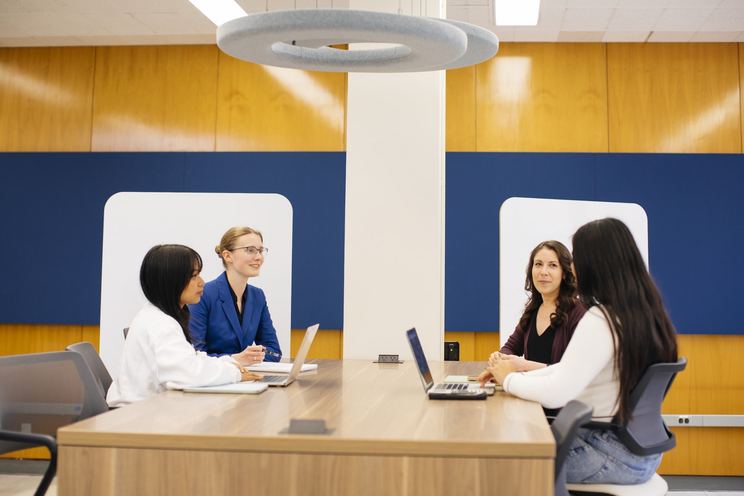 four people sitting around a table with laptops