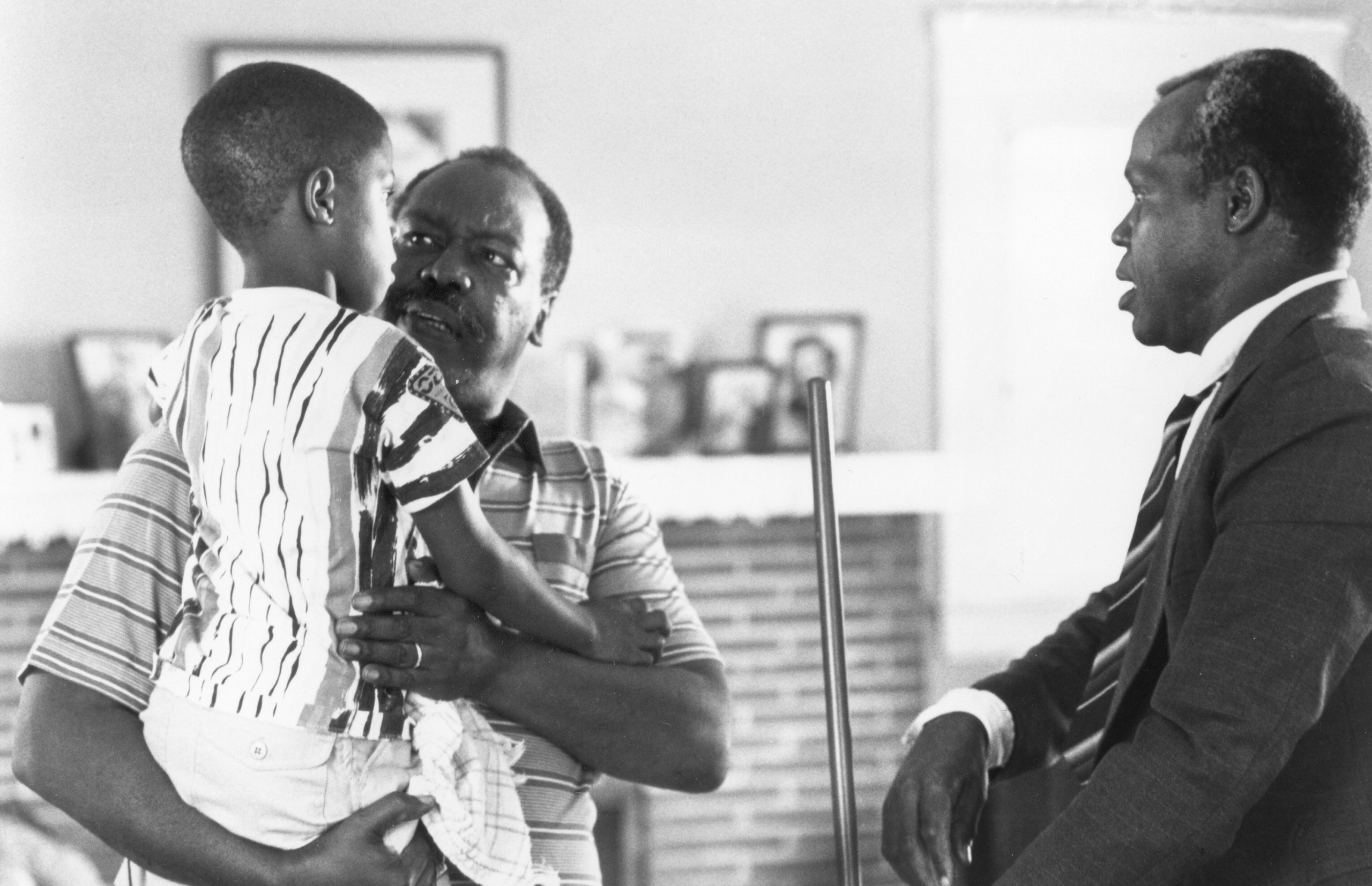 Photo from Ashley Clark Book Talk Program about To Sleep with Anger. Man holding a child while second man gazes at them.
