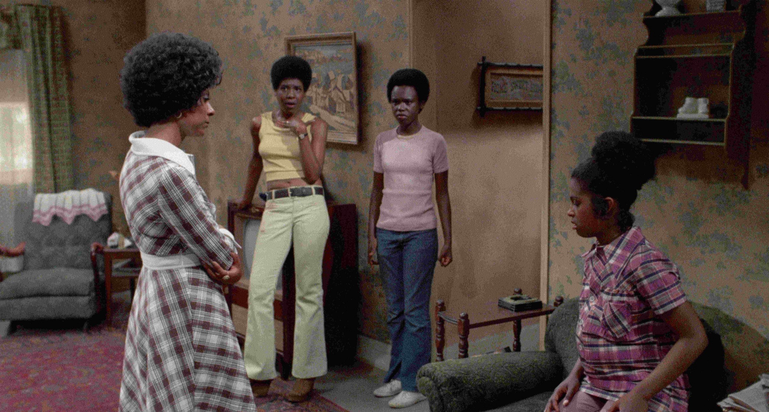 Three women standing while one woman sits