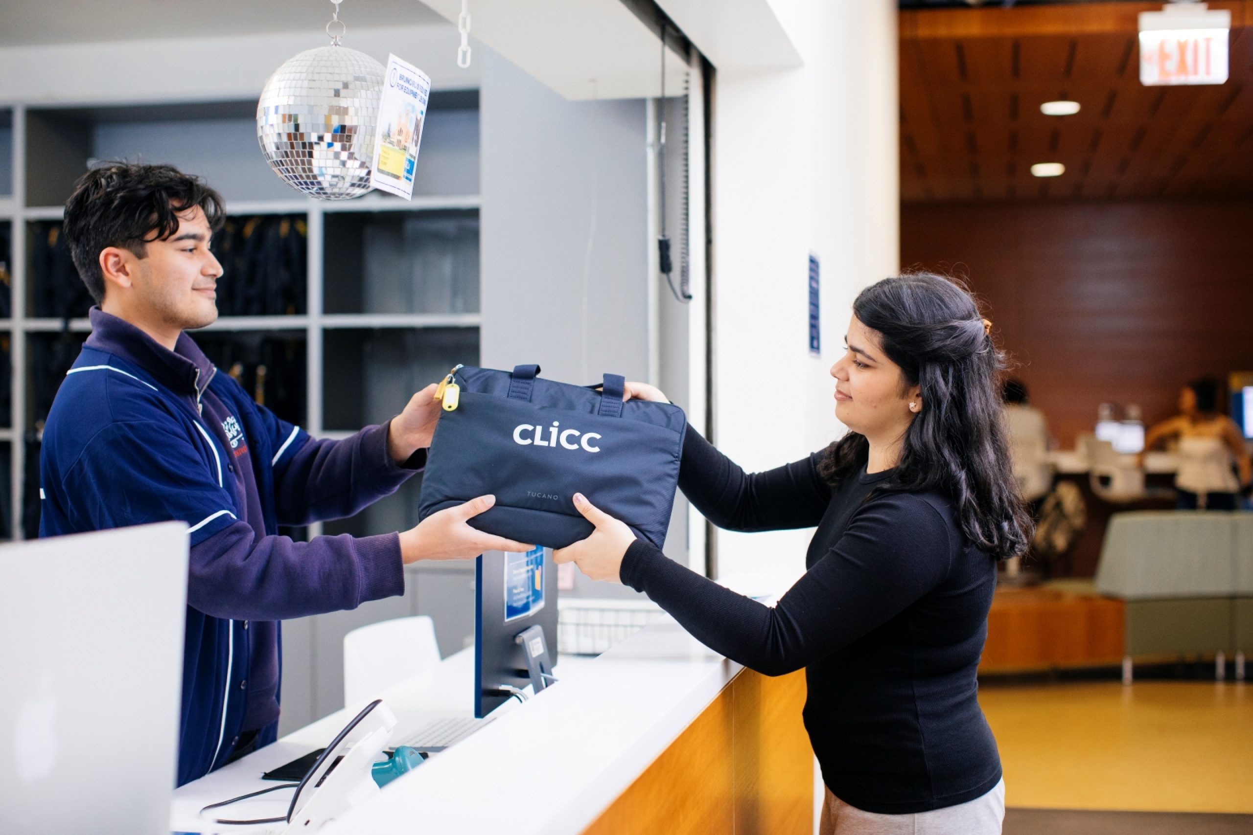 A CLICC student worker handing a laptop to a Library patron.