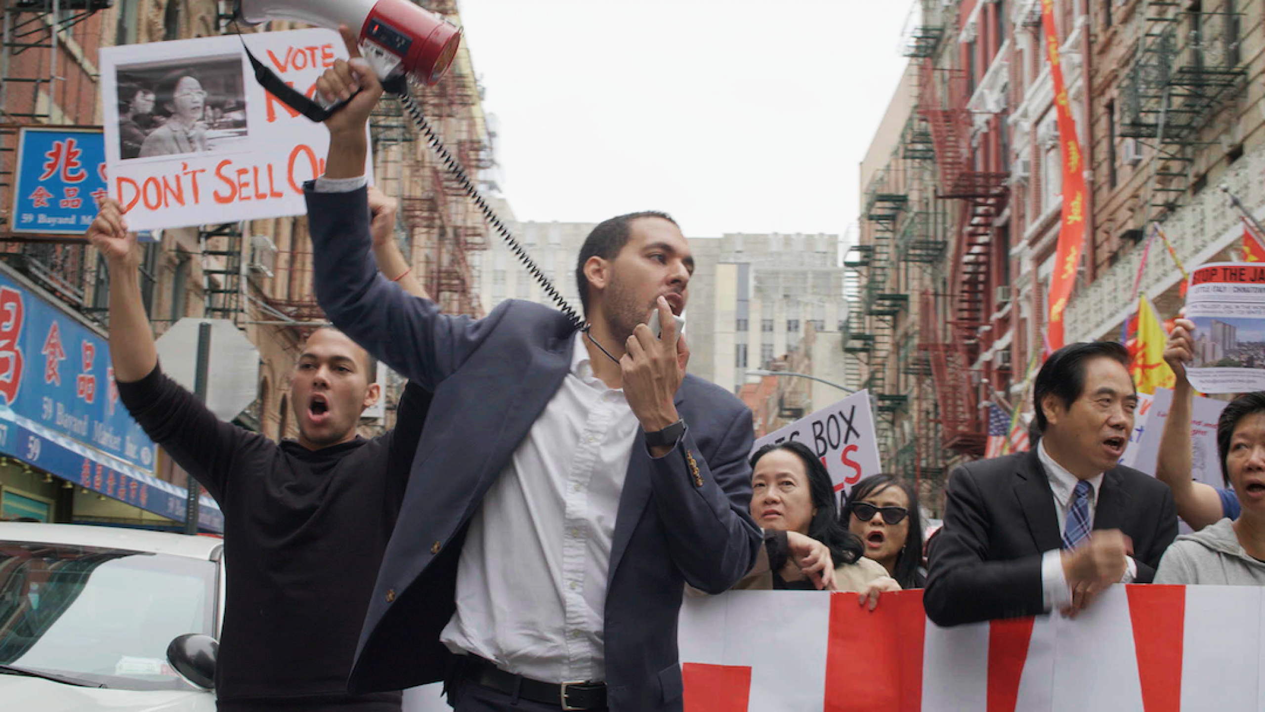 man outside speaking into a megaphone with people behind him