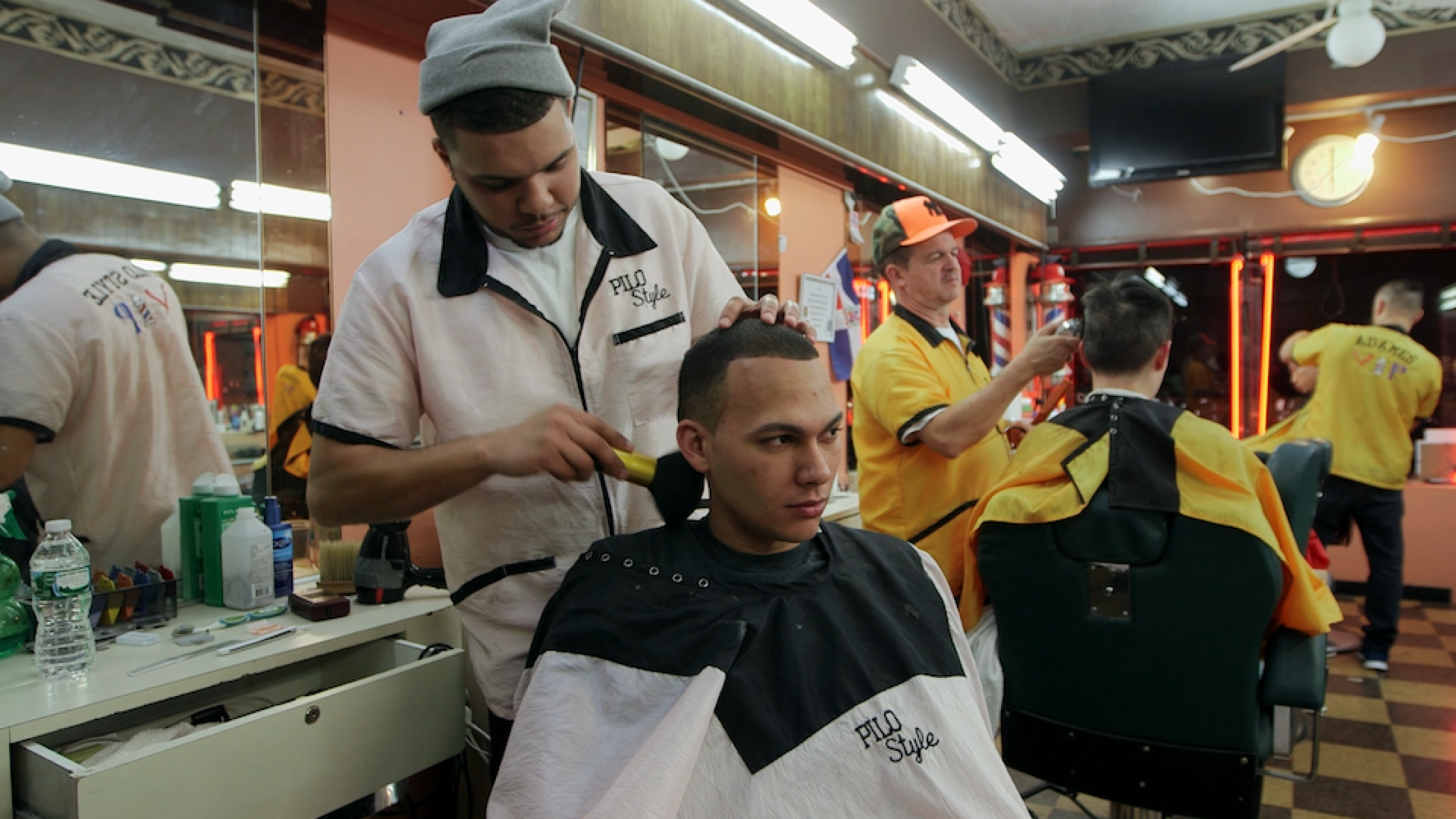 barber and man in barbershop chair with other clients in the background