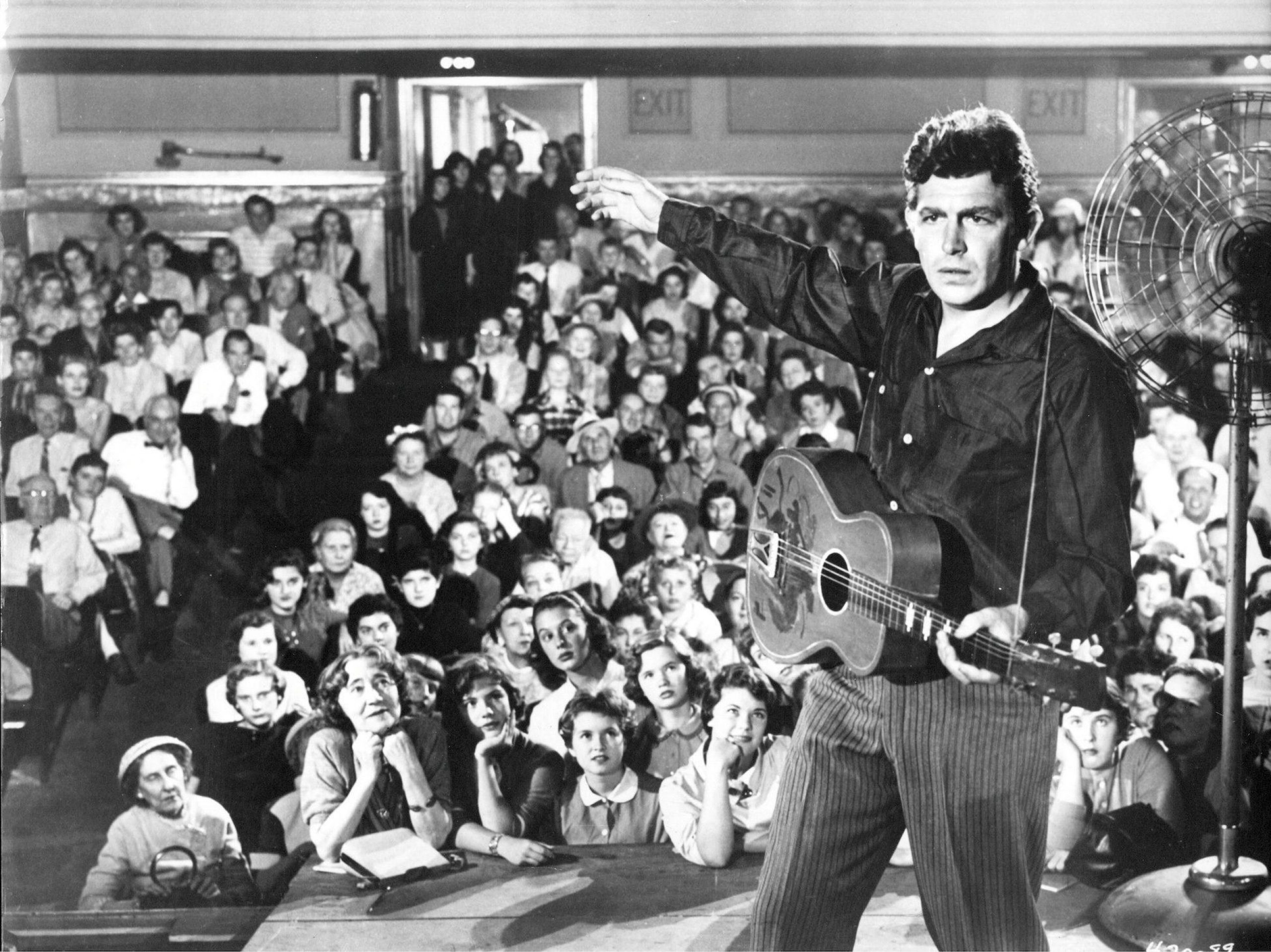 man on stage holding a guitar with an audience of people behind him
