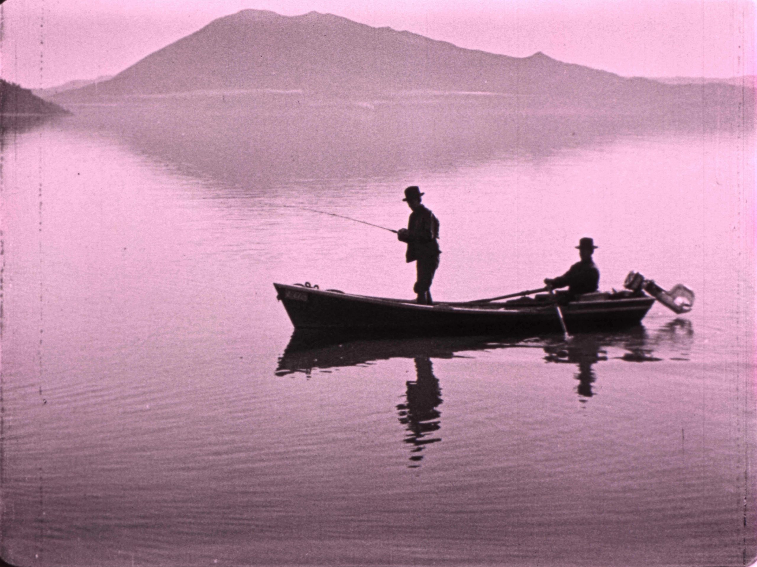 fisherman standing in a boat on the water with another person seated