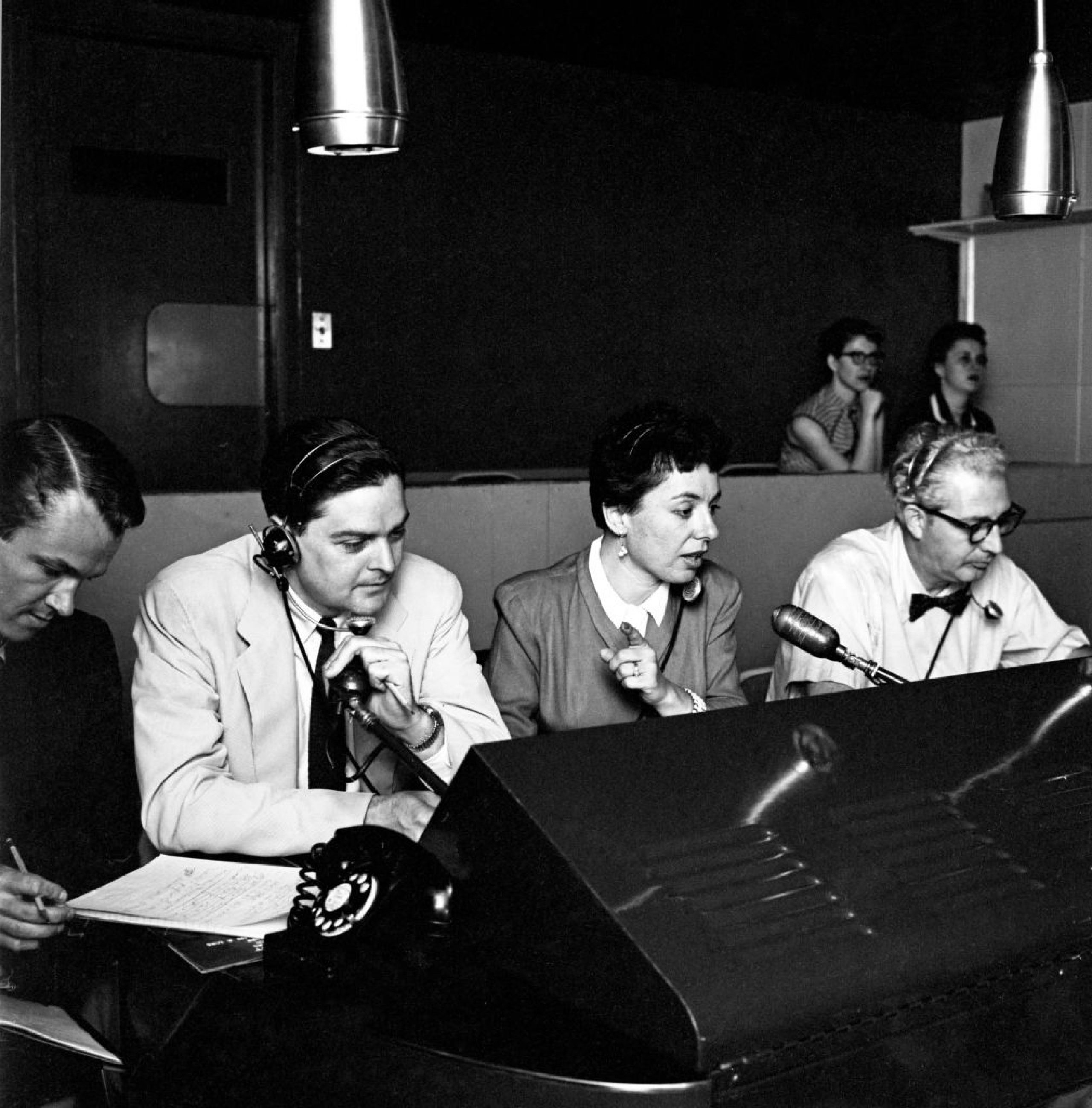 Woman in between two men all seated in front of microphones in a studio