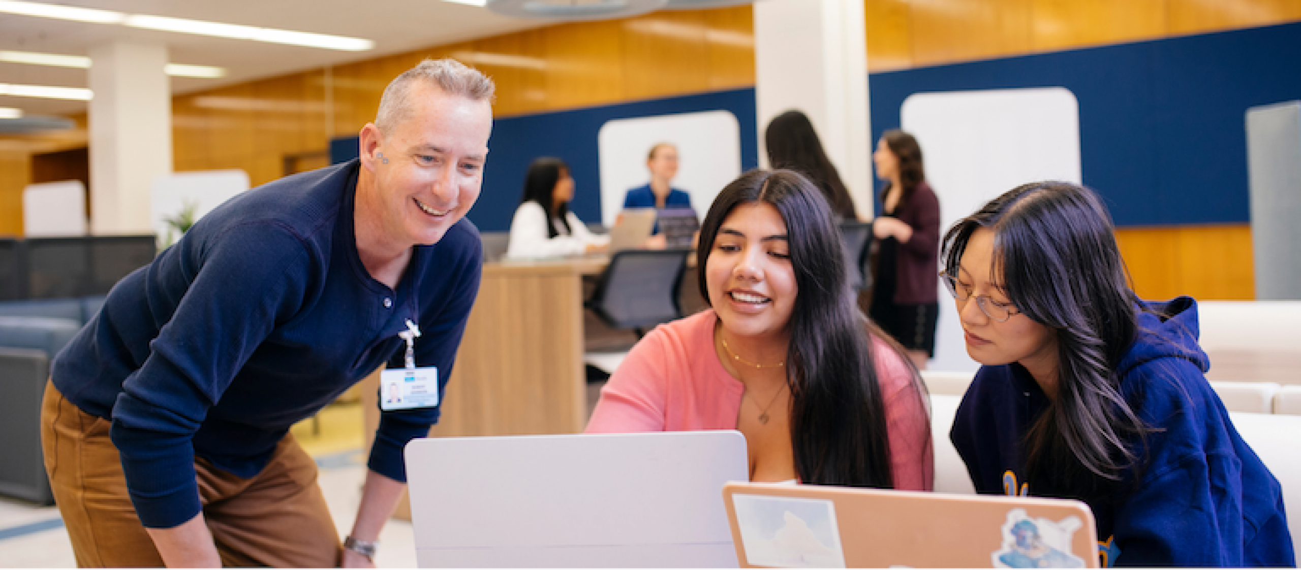 man and two female students in a library all looking at a laptop
