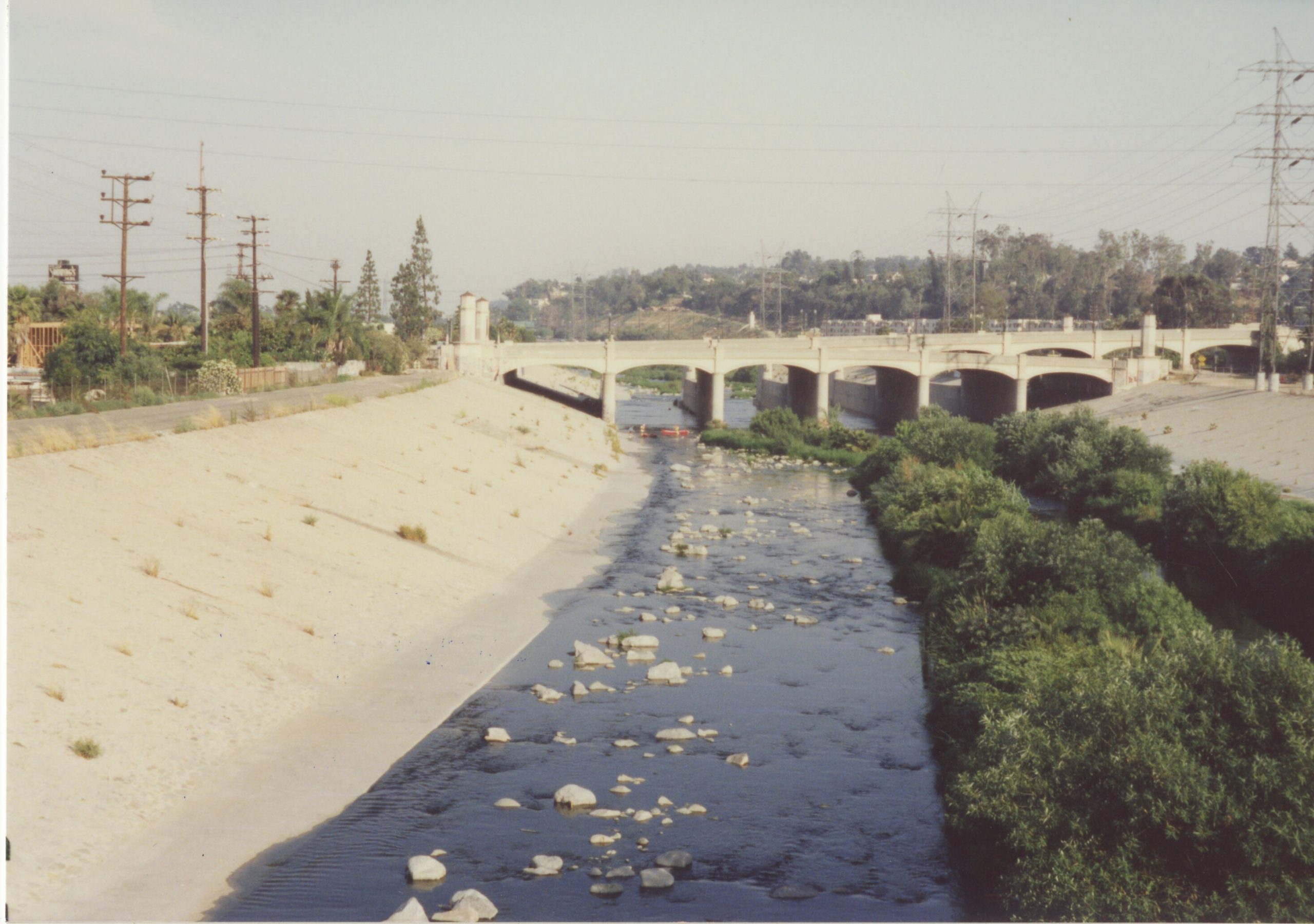Color photo of the LA River facing north and featuring a bridge.