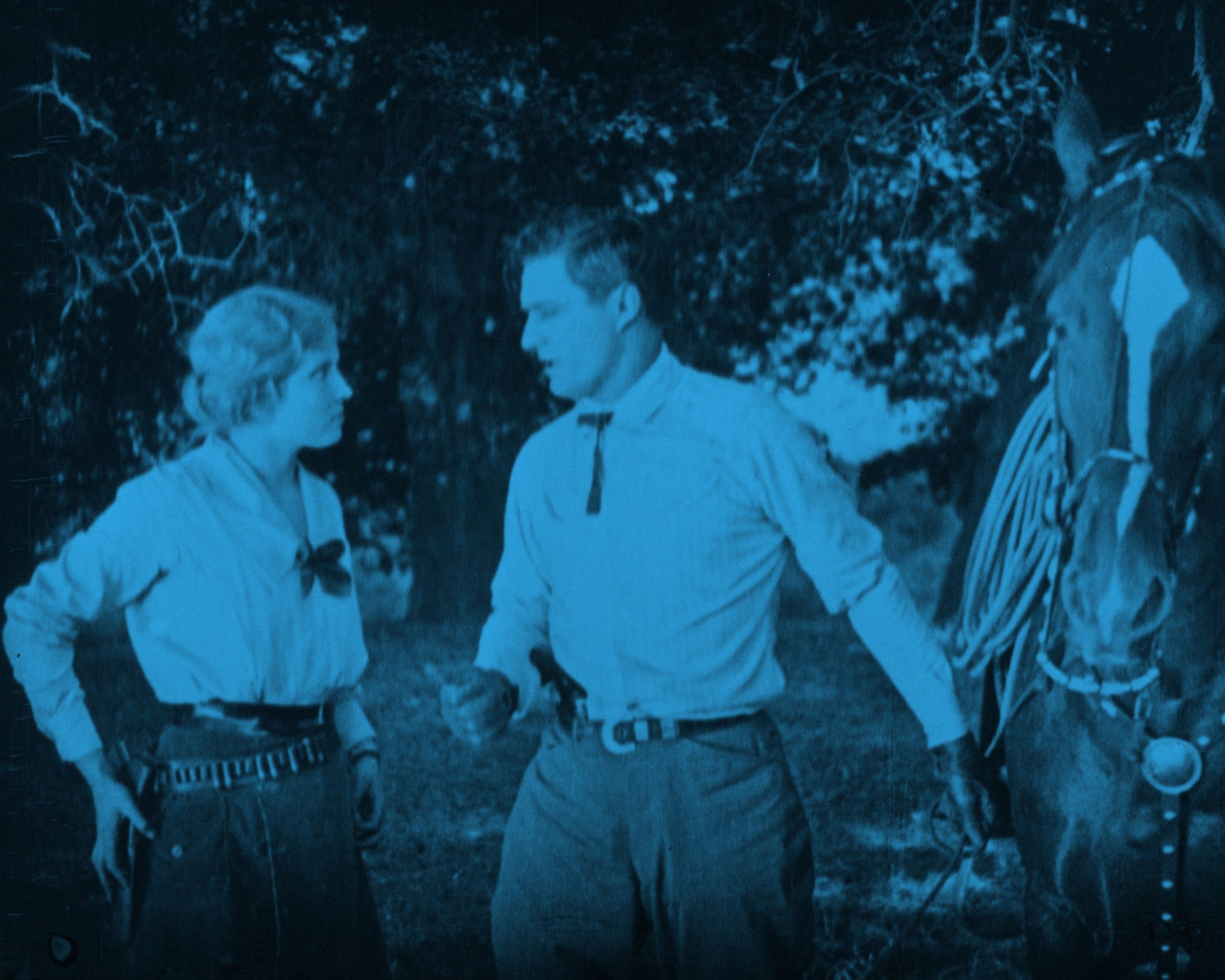 woman in western wear with gun on her hip and man with a horse