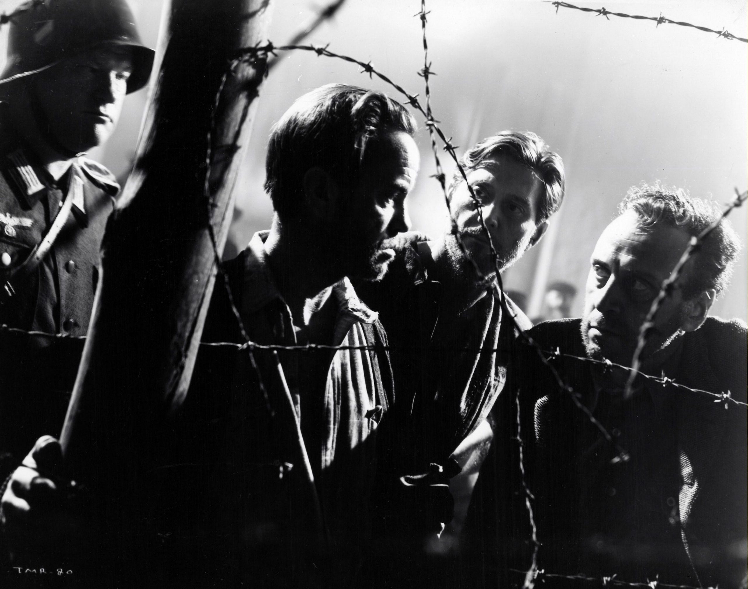 four men standing in front of a barbed wire fence