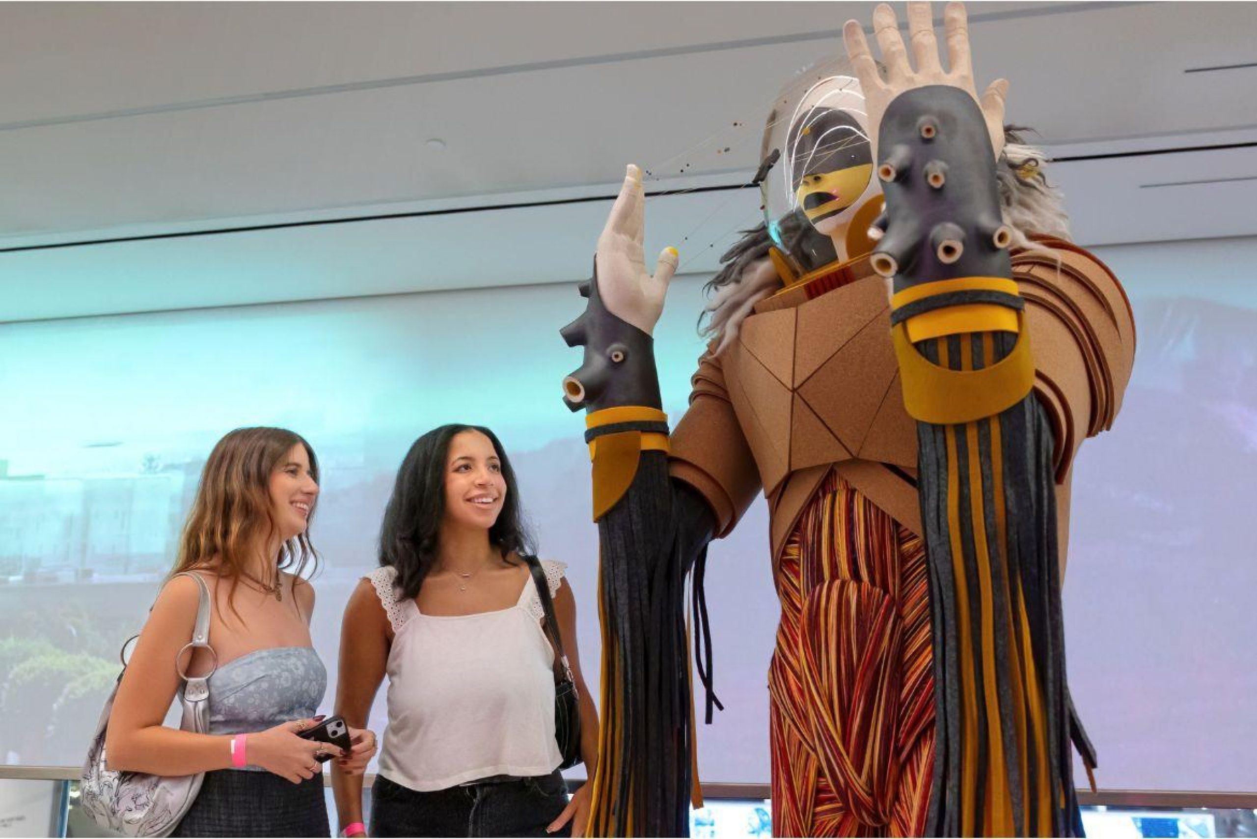 Two women react to “Sovereign,” a large-scale Indigenous figure standing in the Hammer Museum at UCLA lobby.