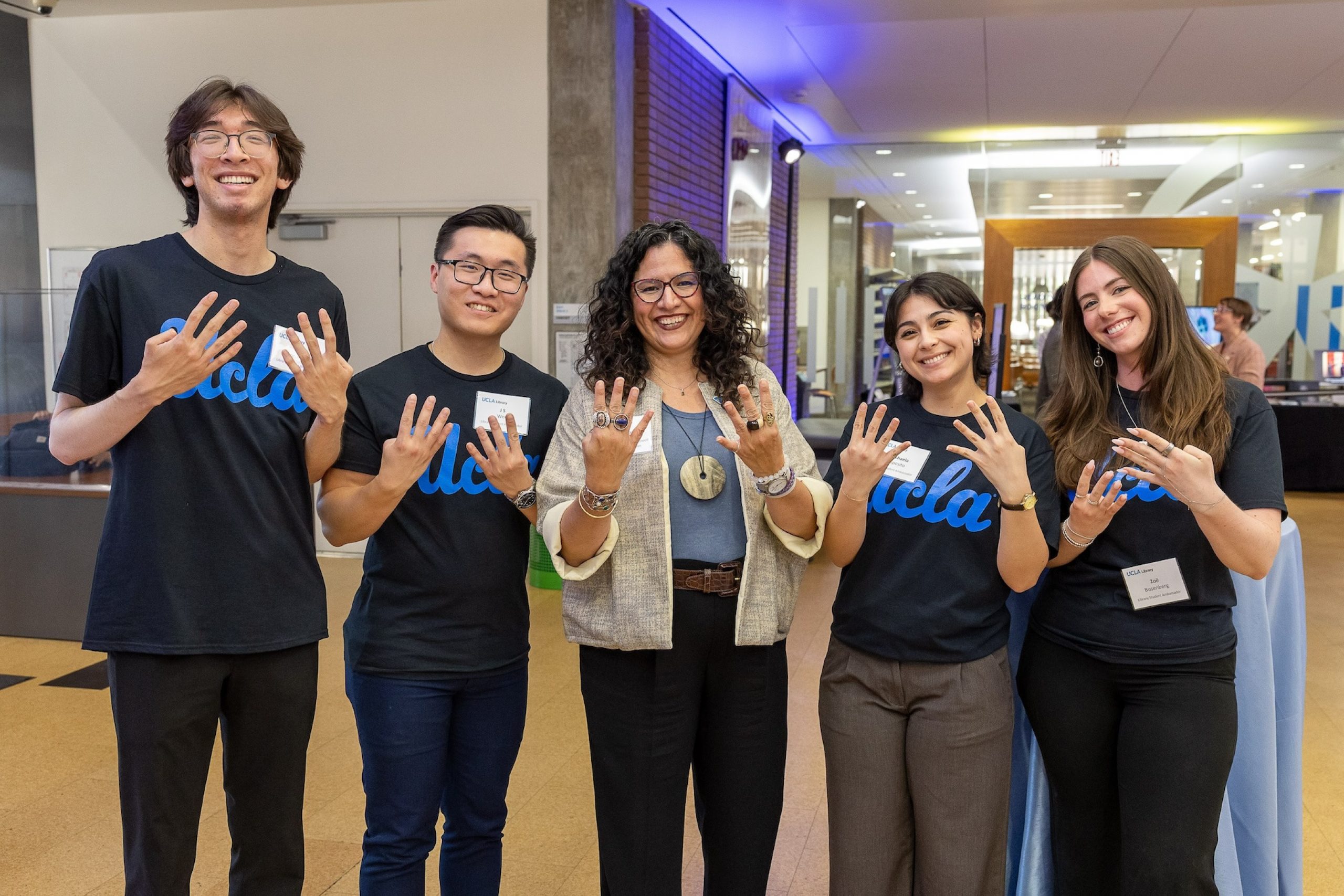 Four students and the university librarian, showing UCLA 8 fingers to represent 8-clap UCLA pride