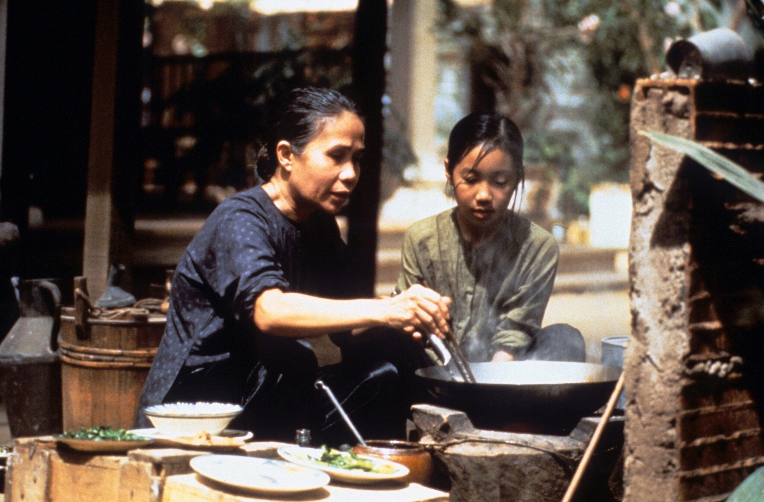 A woman showing her daughter how to cook in an old fashioned large pot