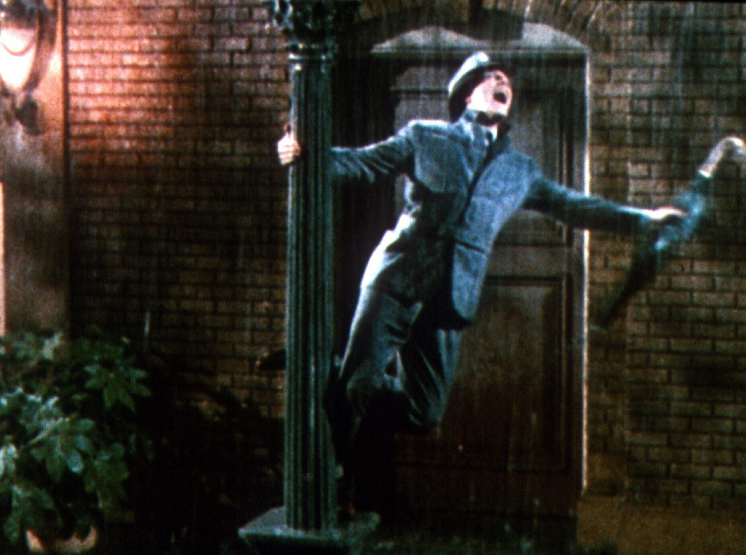 Man holding an umbrella while balancing on a streetlamp in the rain