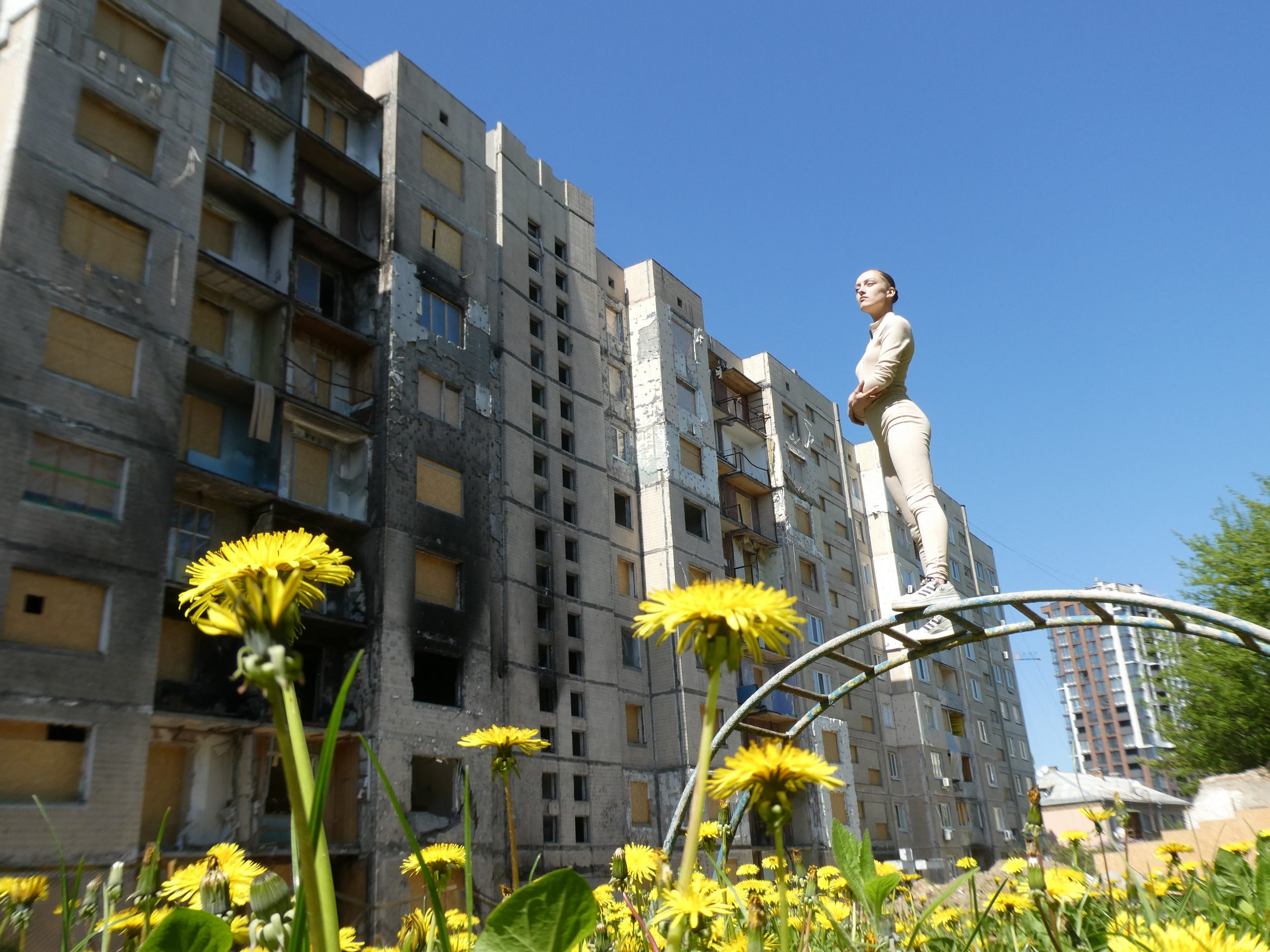 Person balancing on top of a low metal arch in front of a tall building