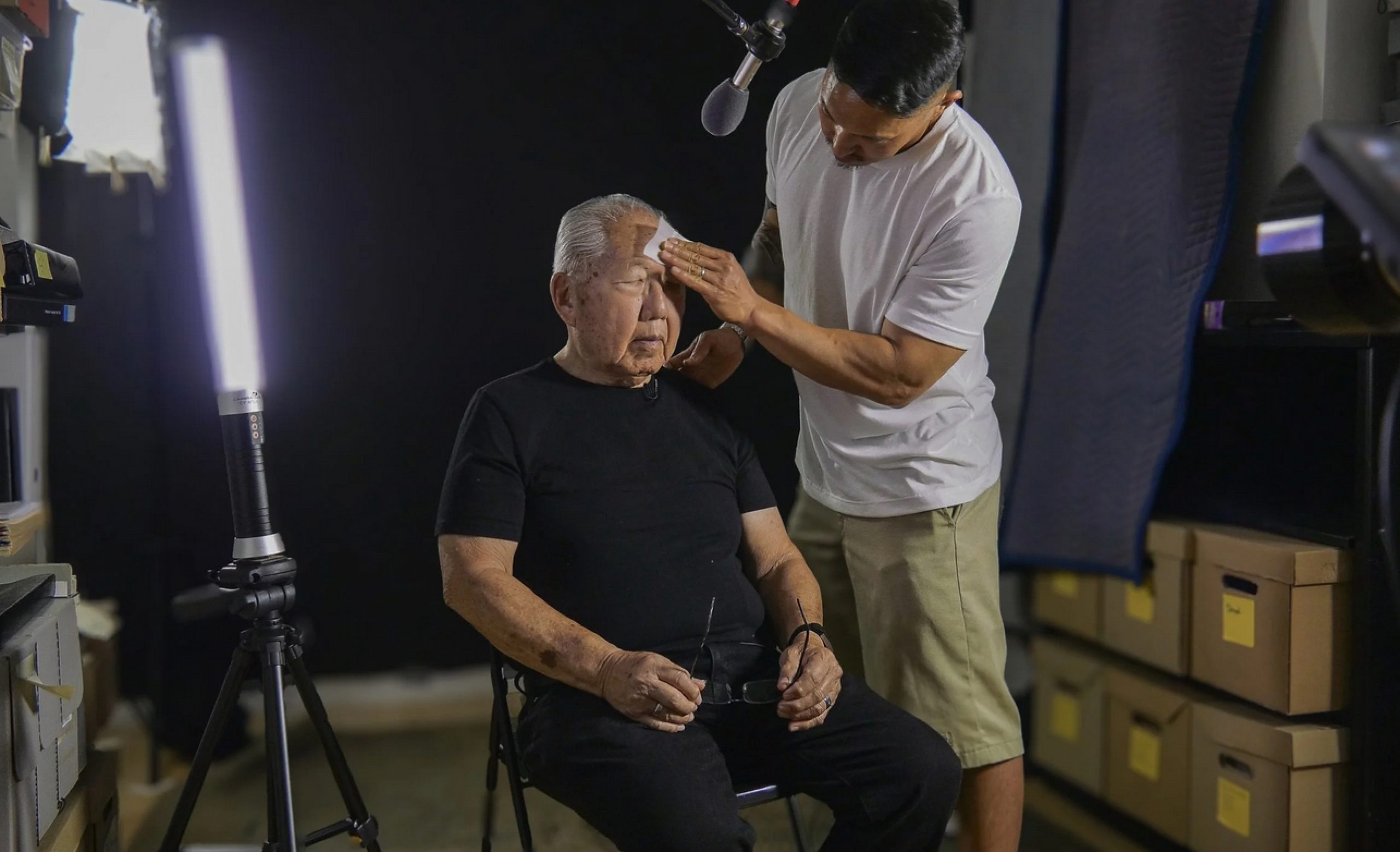 Still from the "Third Act." American filmmaker Robert A. Nakamura sitting on set with man wiping his forehead.