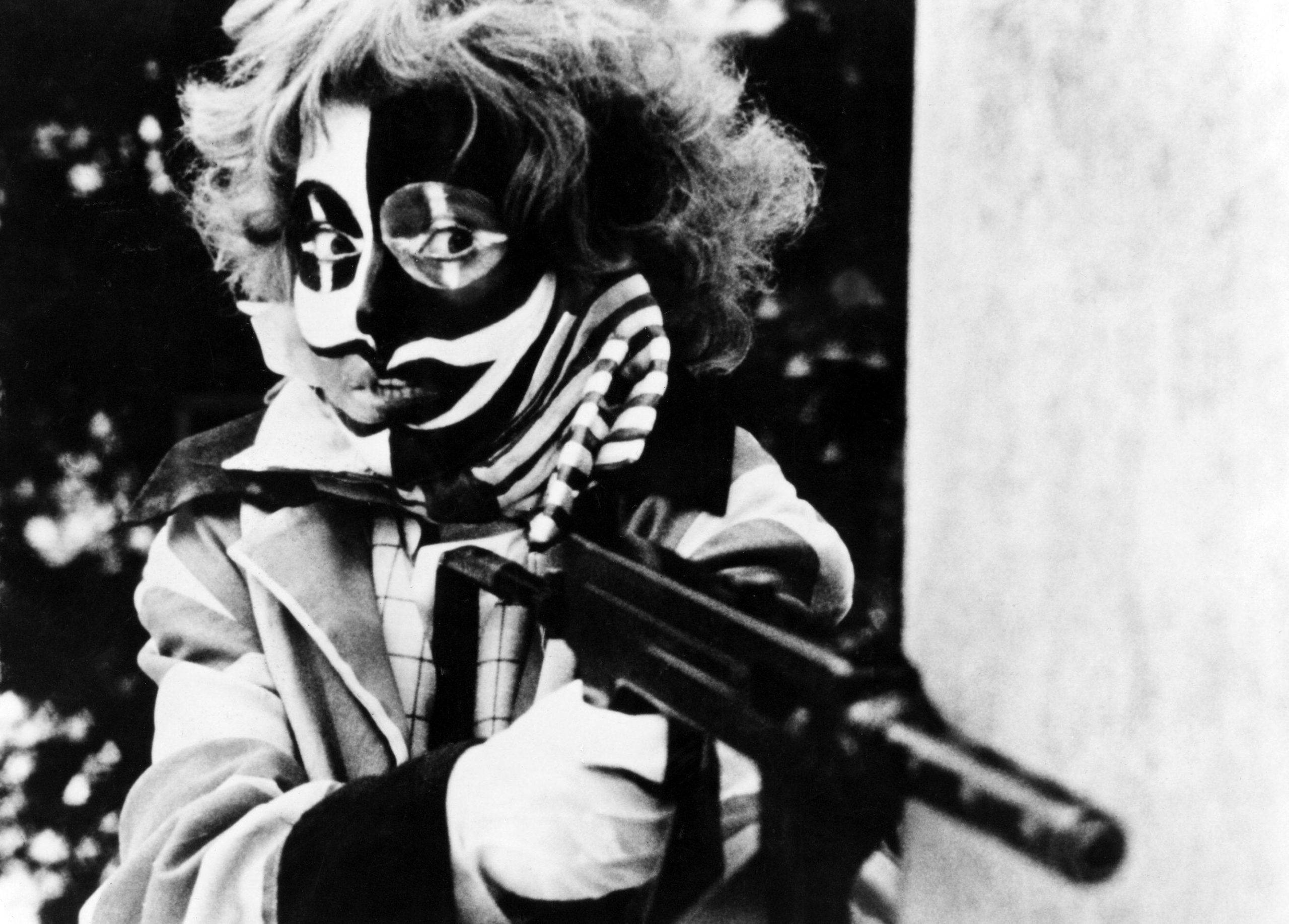 A scary looking person in clown skeleton makeup pointing a rifle
