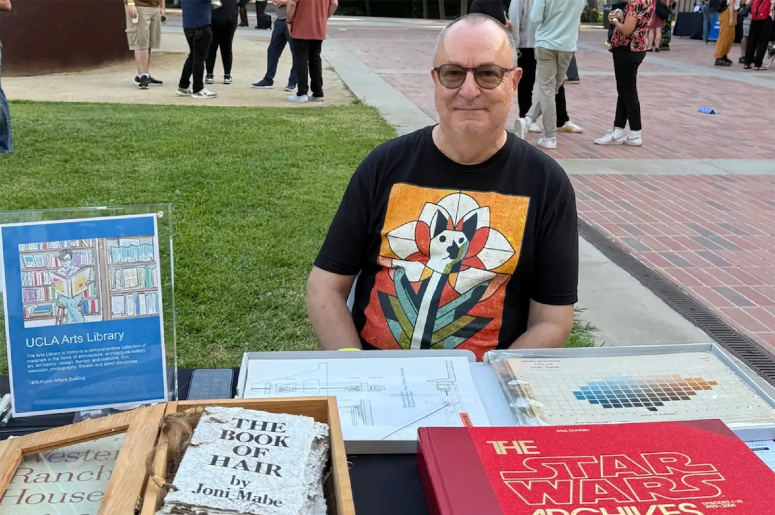 Robert Gore sits outside behind a table display of artists’ books
