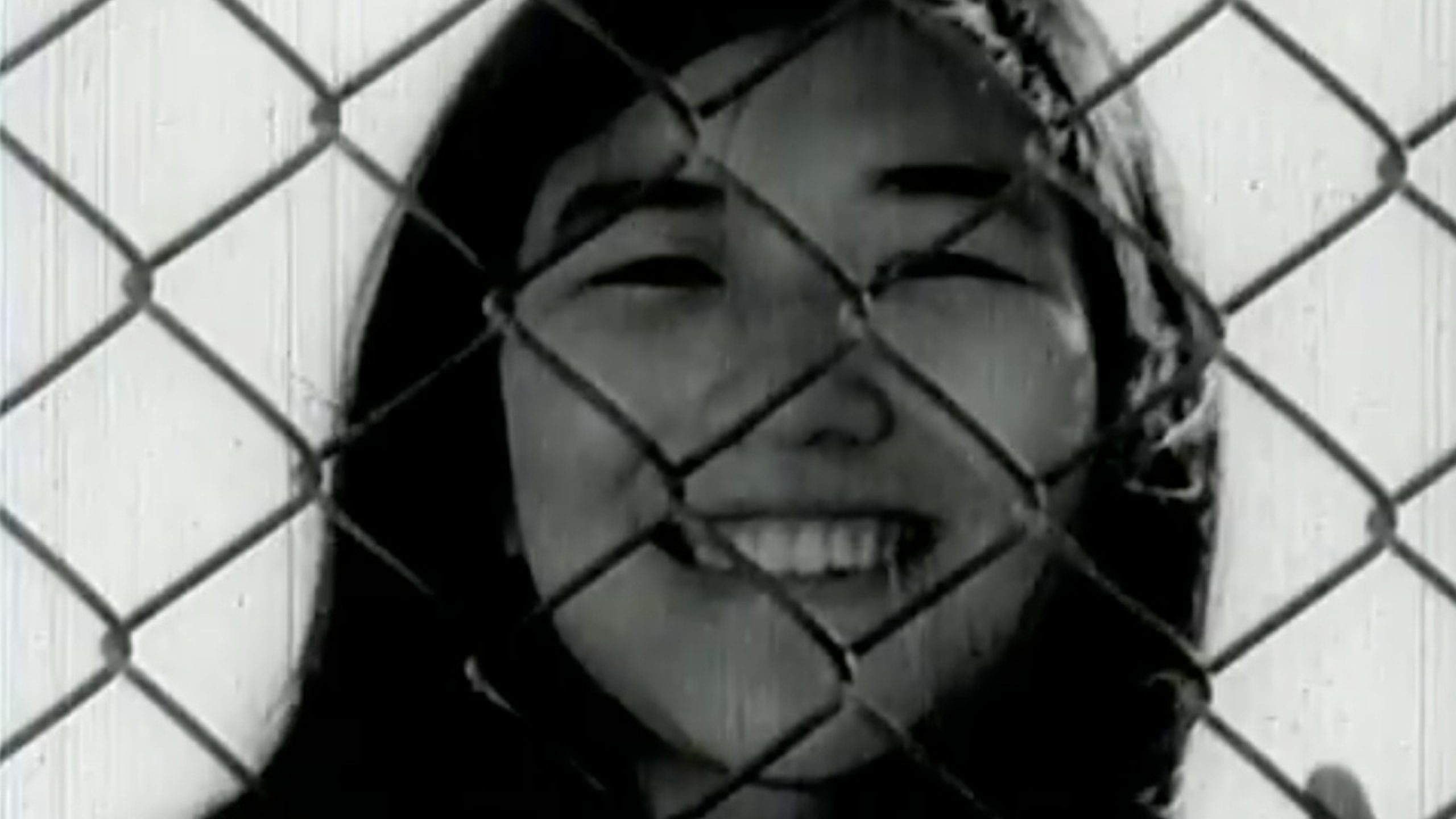 A young girl standing behind a chain link fence