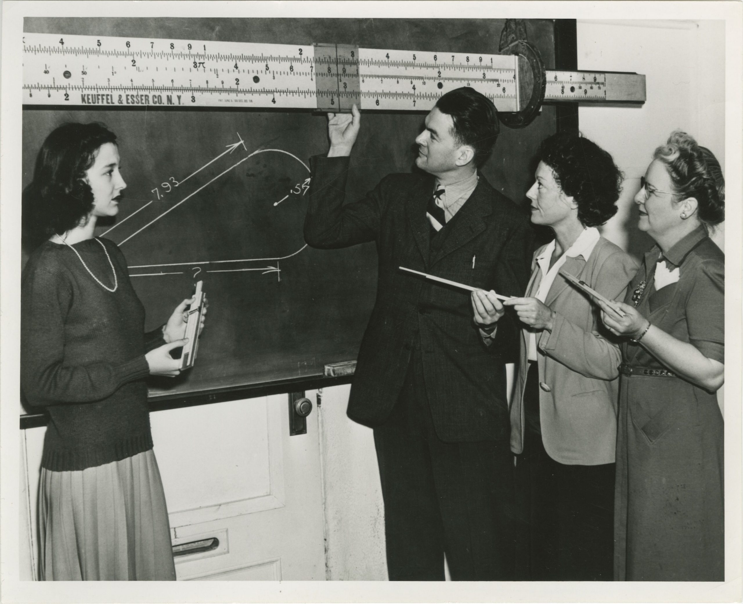 Black and white photograph of Students and professor working with slide ruler on blackboard