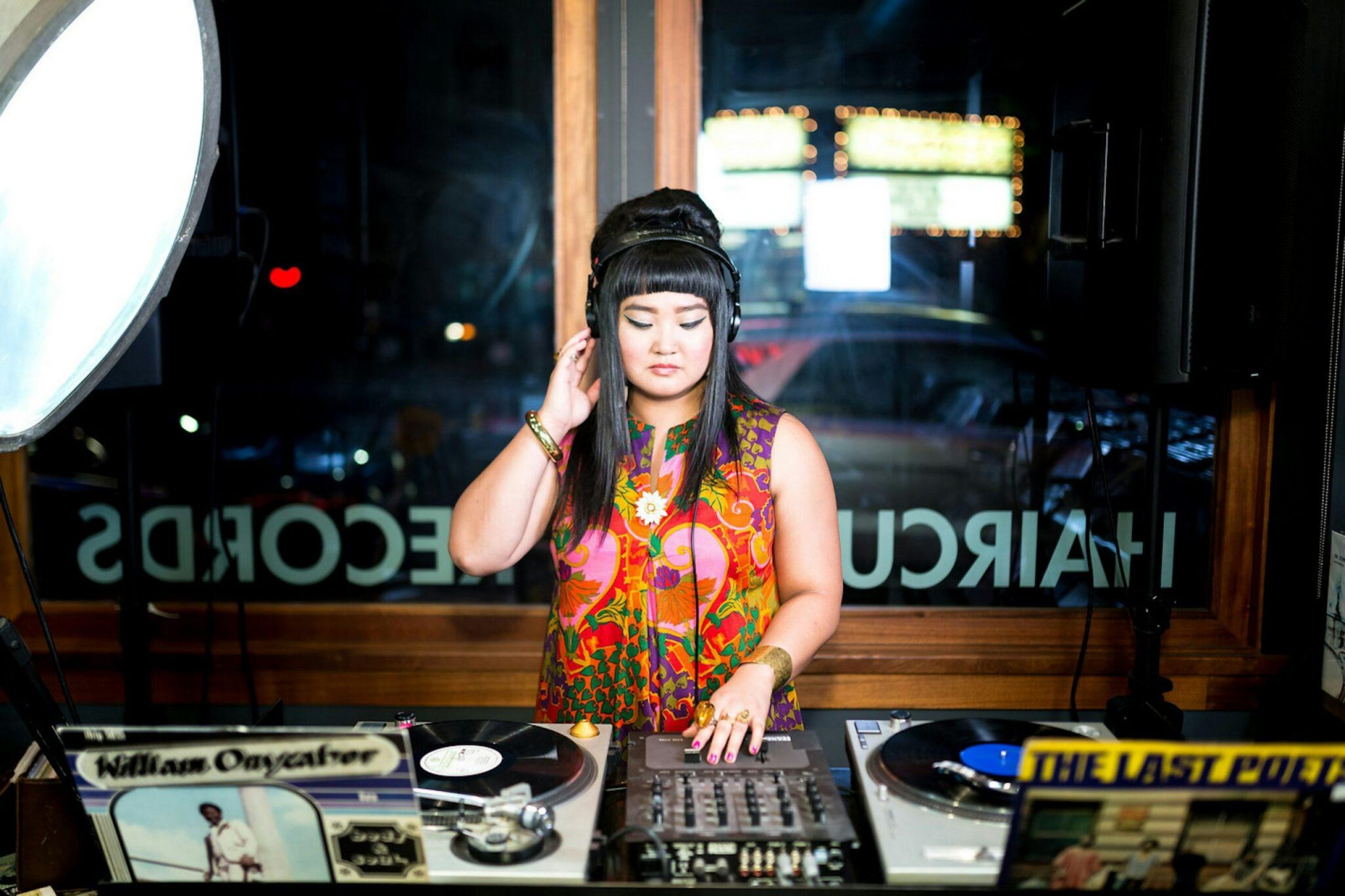 A woman with black hair and colorful floral dress spinning turntables